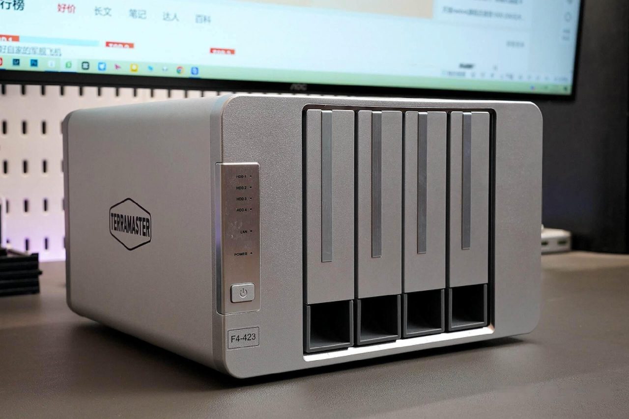 A four-bay aluminium NAS enclosure on a desk with its drive indicators lit