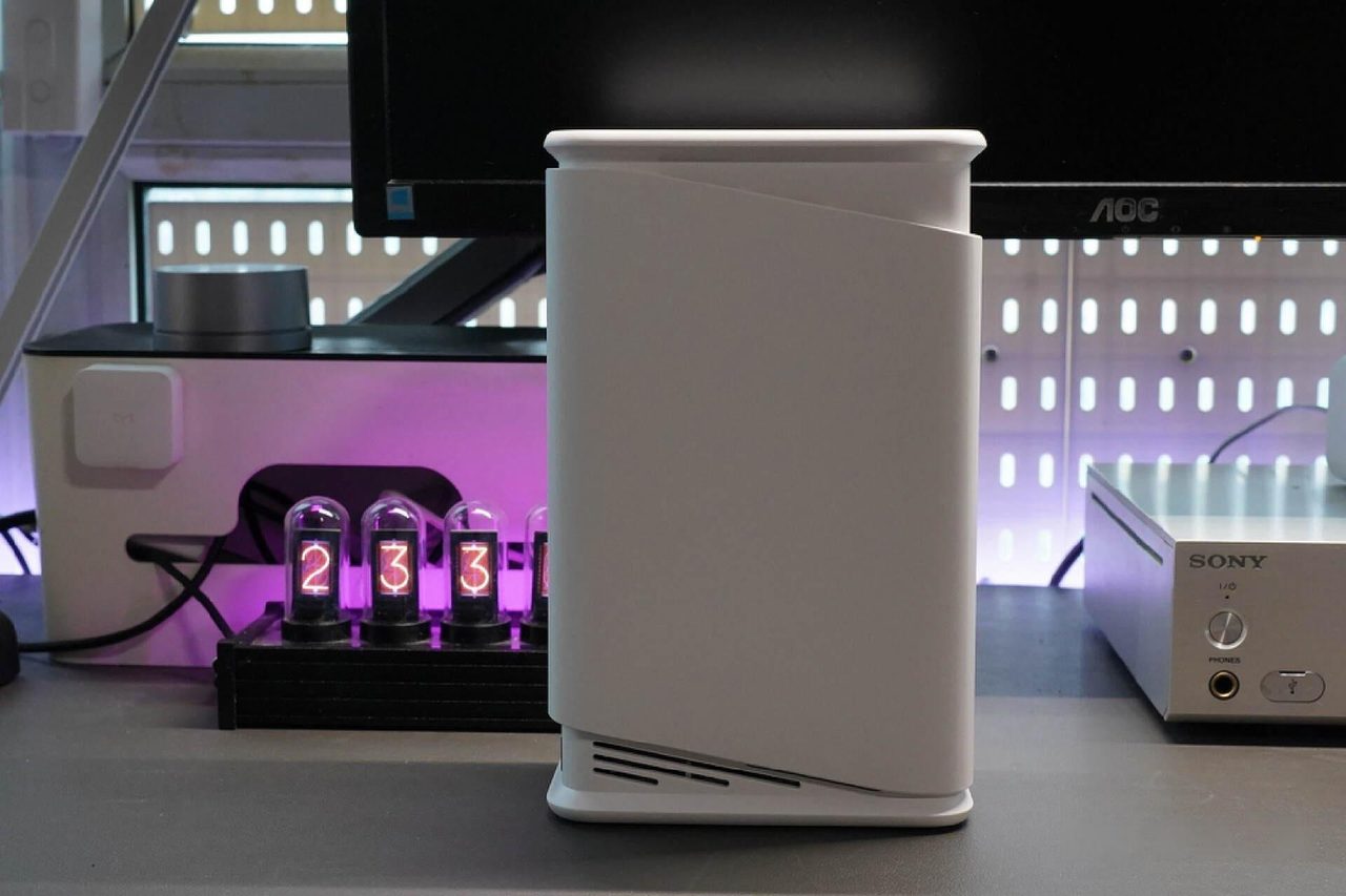 A pale vertical NAS standing on a shelf among other household electronics