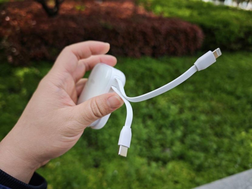 A compact power bank held in the hand with its cable extended