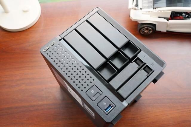 A two-bay NAS enclosure on a wooden desk with a drive sled partly removed